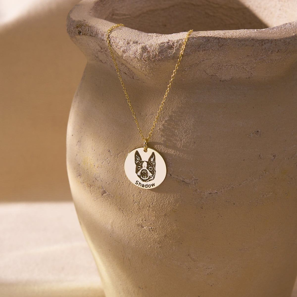 Custom pet portrait necklace with an engraved dog photo on a 14K gold vermeil disc pendant, hanging on a ceramic vase