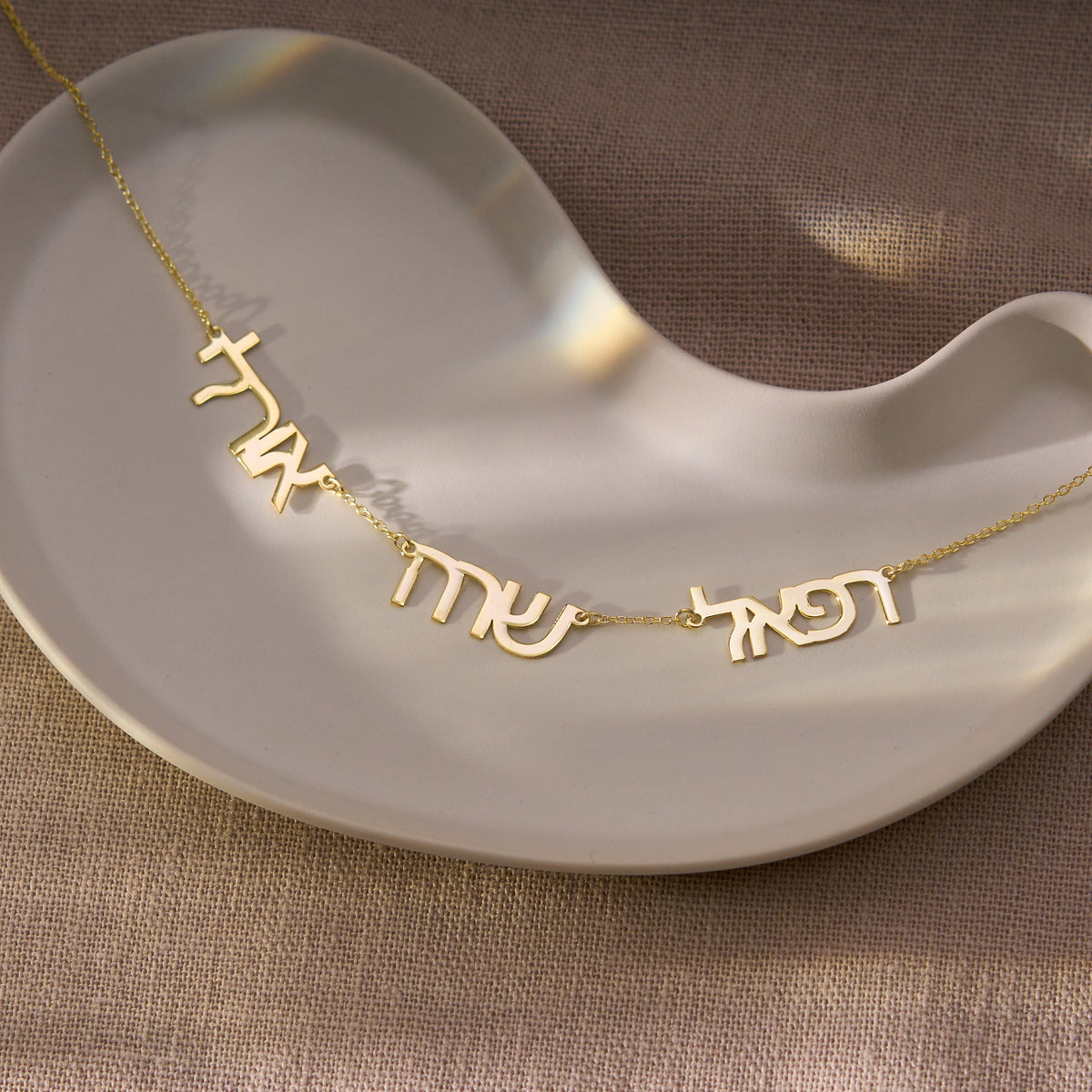 Multiple Hebrew name necklace for up to 4 names, 14K gold vermeil, pendant resting on a ceramic dish