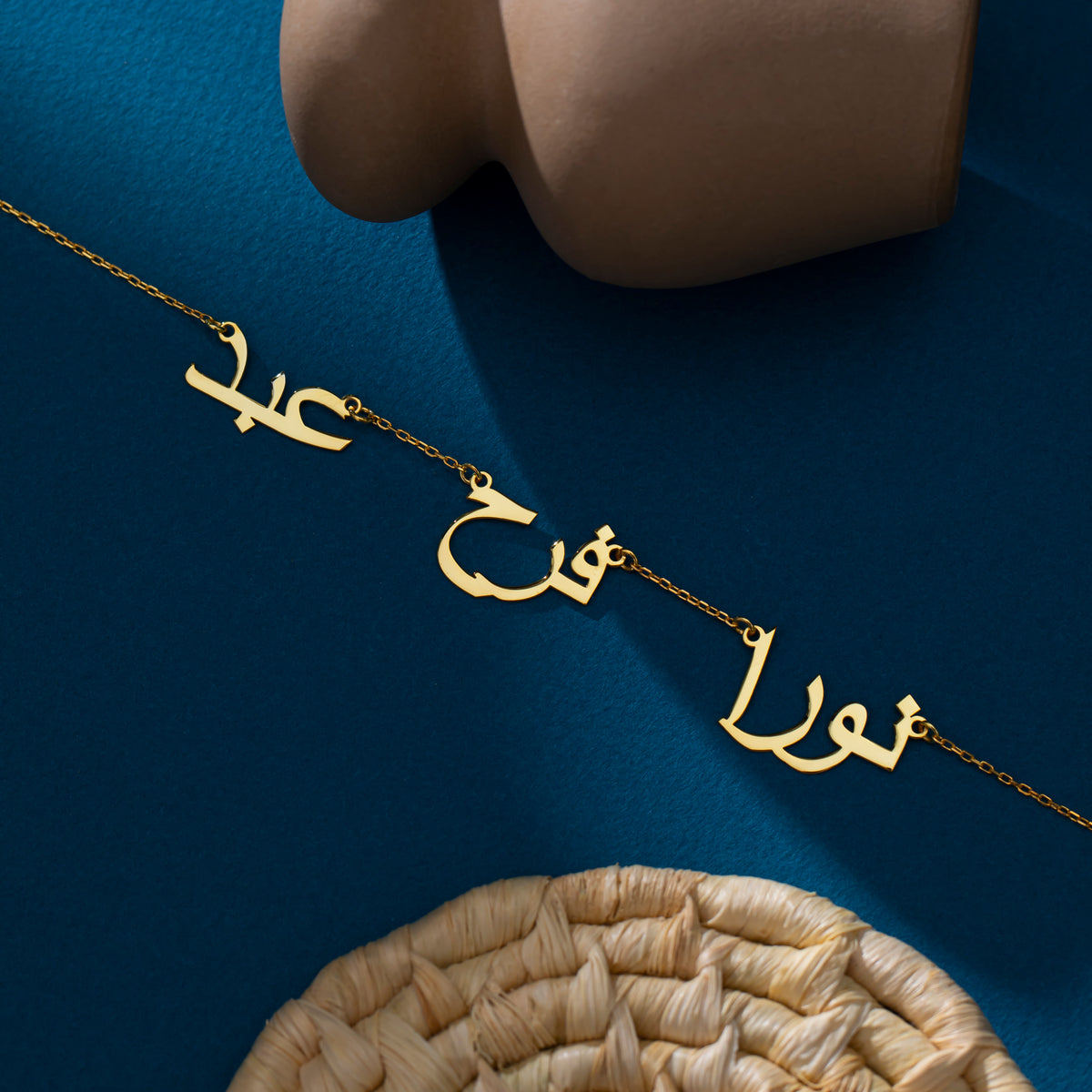 Three-name Arabic necklace, 14K gold vermeil, pendant flat lay on a woven basket (2)
